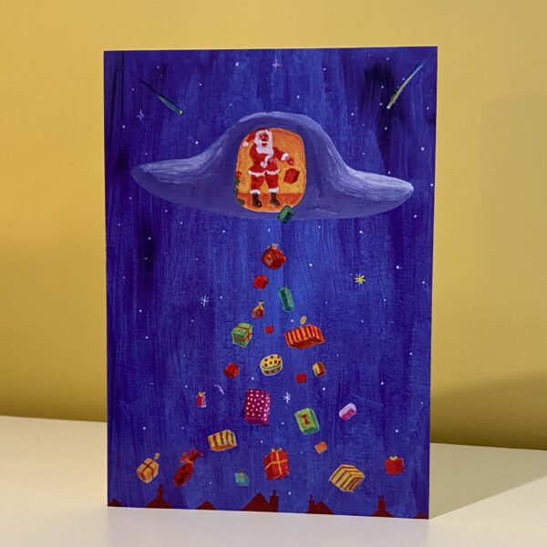 Image is a photograph of a Peter Rodulfo christmas card entitled "Whilst the Town Sleeps" featuring santa/father christmas dropping gifts on a sleeping town from a UFO