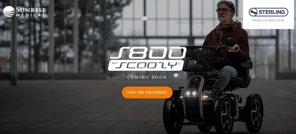 An older man with glasses and a beard rides a rugged, four-wheeled mobility scooter indoors. He wears a brown jacket and scarf. The scooter has large tires, front headlights, and a front basket. Logos for "Sunrise Medical" and "Sterling" appear in the corners. The text "S800 by Scoozy® Coming Soon" is centered, with a bright orange "Keep Me Informed" button below.